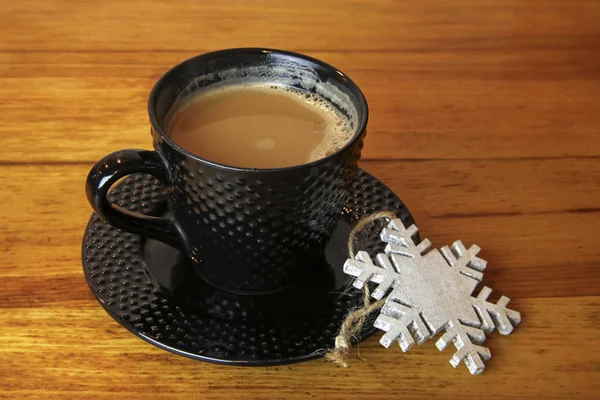 Tasse heißen Kaffee und Weihnachtsstern mit Schneeflocken auf Holztisch — Stockfoto