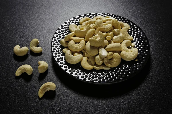 Cashew nuts on plate on black background — Stock Photo, Image