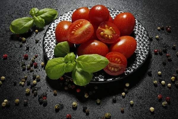 Tomates cerises sur une assiette avec basilic sur fond noir — Photo