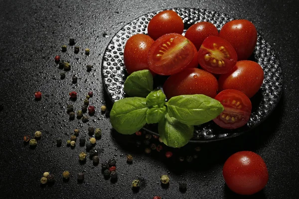 Tomates cerises sur une assiette avec basilic et grains de poivre sur fond noir — Photo