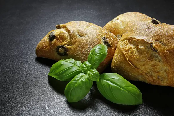 Olive ciabattas with basil leaves on black background — Stock Photo, Image