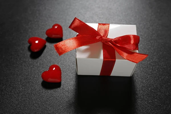 Presente de Valentim com fita vermelha e corações de vidro no fundo preto — Fotografia de Stock