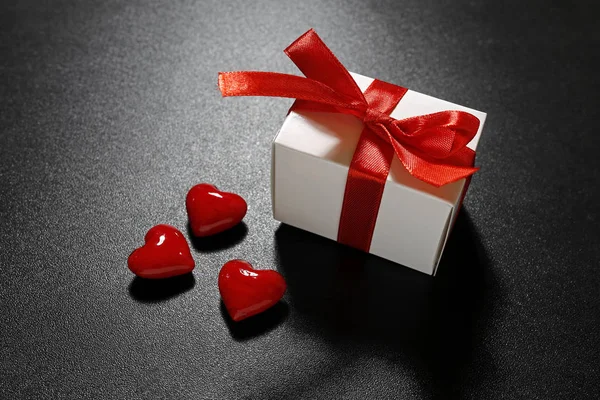 Подарок Валентина с красной лентой и стеклянными сердцами на черном фоне — стоковое фото