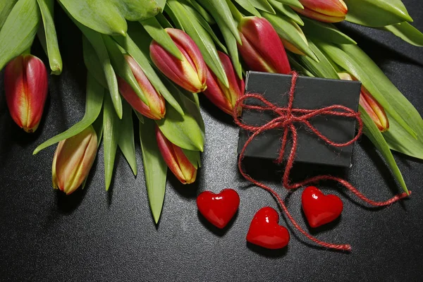 Tulipas, caixa de presente e corações vermelhos no fundo preto — Fotografia de Stock