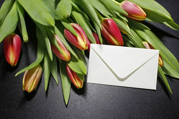 Buquê de tulipas e envelope branco sobre fundo preto — Fotografia de Stock