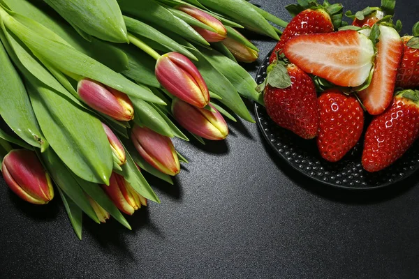 Tulips and fresh strawberries on black background — Stock Photo, Image