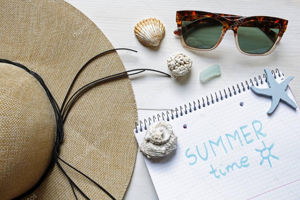 summer time concept- straw hat, seashells, sunglasses and notebook on white wooden background