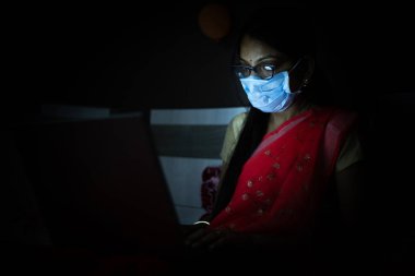 Gece geç saatlere kadar dizüstü bilgisayarıyla çalışan maskeli genç Hintli kadın, evden çalışan serbest çalışan. Coronavirus, Covid-19. Evde kal. Güvende ol. Karantinadaki kadın..