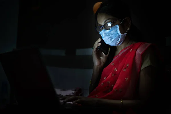 Gece geç saatlere kadar dizüstü bilgisayarıyla çalışan maskeli genç Hintli kadın, evden çalışan serbest çalışan. Coronavirus, Covid-19. Evde kal. Güvende ol. Karantinadaki kadın..