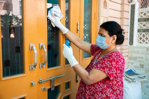 Coronavirus. Koronavirüs salgını sırasında yüz maskesi temizleyen ve evinin kapısını dezenfekte eden bir kadın. COVID-19 enfeksiyonunun önlenmesi. Koronavirüsün yayılmasını engelle.