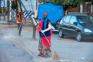 Jodhpur, Rajashtbn, India. 30 March 2020: A woman sweeping the city road in the morning manually with a traditional broom.Coronavirus, covid-19 situation. clipart
