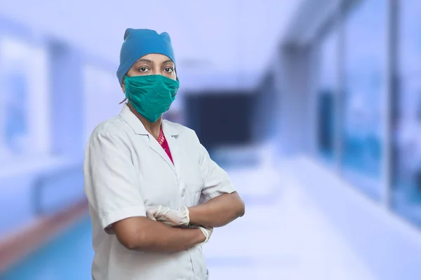 Cerrahi maske takan ve kaptanı hastane koridorunun dışında çapraz duran kadın doktor portresi. Covid-19, Coronavirüs Salgını.