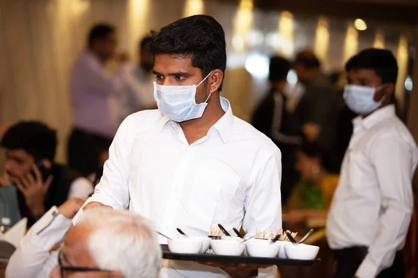 Jodhpur, Rajasthan, Hindistan - 10 Mart 2020: Covid-19 virüsü ve Coronavirus konsepti. Garsonlar cerrahi maske takarak bir restoranda yemek servisi yapıyorlar. Hindistan 'da Covid-19 virüs salgını.