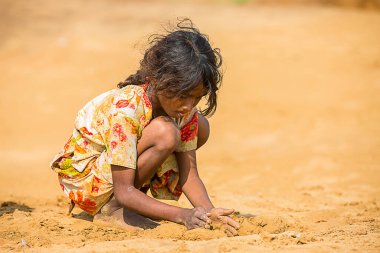 Jodhpur, Rajasthan, Hindistan - 18 Haziran 2019: Sıcak yazda kumla oynayan fakir kırsal kız, imtiyazsız Hintli yoksul çocuklar.