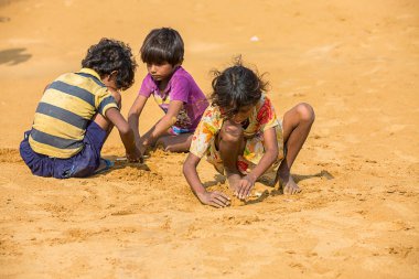 Jodhpur, Rajasthan, Hindistan - 18 Haziran 2019: Sıcak yazda kumla oynayan fakir kırsal çocuklar, imtiyazsız Hintli çocuklar.