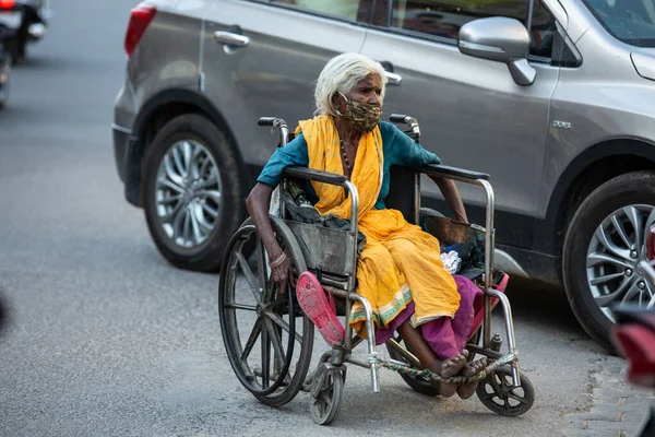 Jodhpur, Rajasthan, Hindistan - 20 Mayıs 2020: Tekerlekli sandalyede oturan, maske takan zavallı, engelli yaşlı kadın, tecrit krizi sırasında yolda geziniyor, yiyecek bir şey yok, gidecek yer yok.
