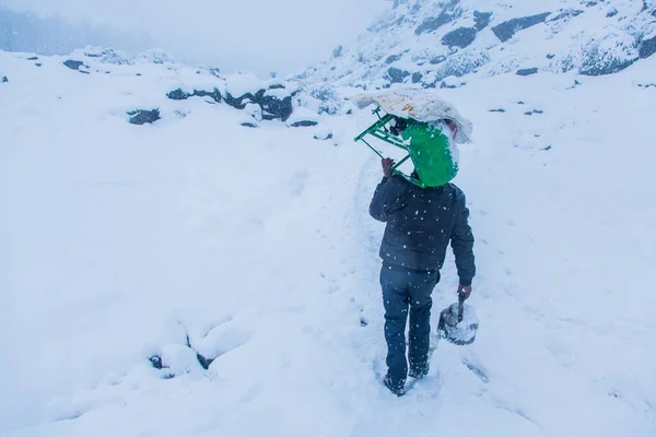A man walking in heavy snow lifting green stove on his shoulder, bizarre conditions - Image — Stock Image Man Walking Heavy Snow Lifting Green Stove His Shoulder Bizarre Royalty Free Stock Images