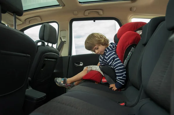 Little boy faste seat belt in high back booster car seat. Child safety.