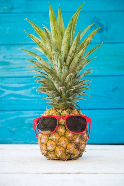 Piña de vacaciones tienen gafas de sol sobre fondo de madera azul — Foto de Stock