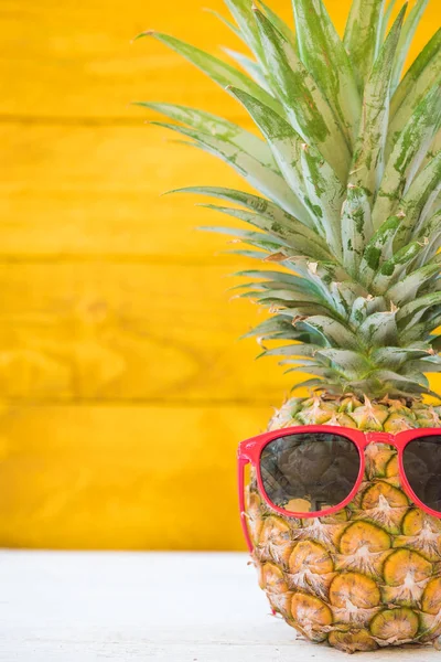 Праздничные ананасы имеют солнечные очки на желтом деревянном фоне — стоковое фото