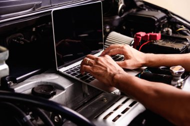 Atölyede dizüstü bilgisayarla çalışan profesyonel araba tamiri ya da bakım motoru servisi