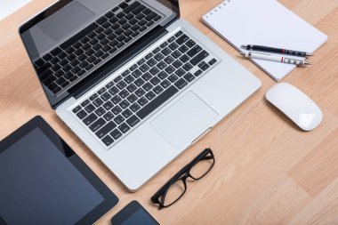 Dijital tabletli ve ahşap masadaki beyaz akıllı telefonlu üst görünüm açık dizüstü bilgisayar