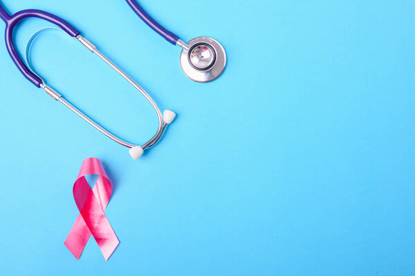 Breast cancer month concept, flat lay top view, pink ribbon and stethoscope on blue background with copy space for your text