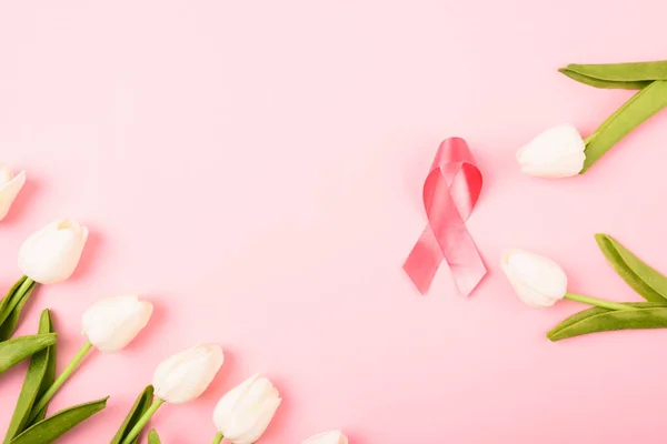 Breast cancer month concept, flat lay top view, pink ribbon and Tulip Flower on pink background with copy space for your text