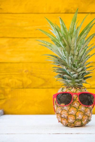 Праздничные ананасы имеют солнечные очки на желтом деревянном фоне — стоковое фото