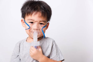 Kapalı Asyalı yüz, küçük çocuk hasta buhar spreyi nebulizer maskesi kullanıyor beyaz arka planda kendini soluyor, sağlık hizmetleri...