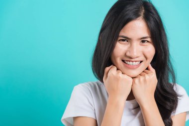 Asyalı güzel, mutlu, güzel bir kadın tişört giyiyor. İki elini çenenin altında tutuyor. Gülümsüyor.