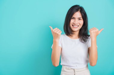 Asyalı güzel mutlu kadın gülümse beyaz dişli beyaz tişört giy başarılı kadın iki baş parmak işareti yapıyor, mavi arka planda fotokopi alanı olan