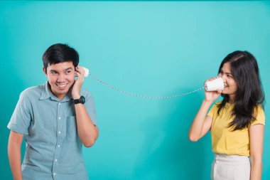 Asyalı mutlu genç çift güzel bir gülümseme ve kağıt ile birlikte konuşmak mavi arkaplanda fotokopi alanı ile bir stüdyoda telefon edebilirler.