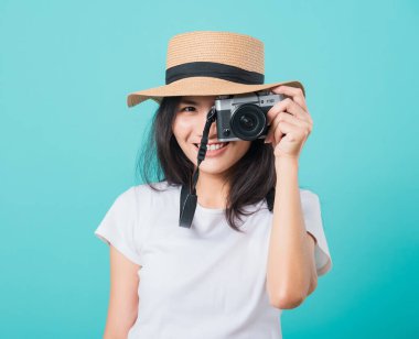 Gezgin turist mutlu Asyalı genç kadın yaz şapkasıyla gülümsüyor aynasız fotoğraf makinesiyle duruyor, mavi arkaplanda fotokopi alanı ile fotoğraf çekiyor.