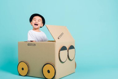 Mutlu Asyalı çocuk araba sürerken gülümse. Karton kutu hayal gücü, yaz tatili seyahat konsepti, mavi arkaplanda metin alanı için fotokopi alanı olan bir stüdyo.