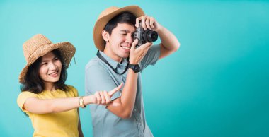 Mutlu Asyalı çift heyecanlı genç kadın işaret parmağı ve yaz tatilinde fotoğraf çeken yakışıklı adam. Turistler mavi arka planda izole edilmiş ve metin alanı için fotokopi çekiyorlar.