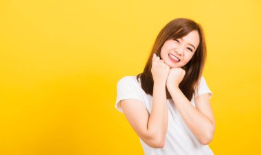 Asyalı mutlu bir portre güzel, genç bir kadın tişört giyiyor. Mutlu bir ifade. Yumruk çenenin altına bastırılmış, izole edilmiş kameraya bakıyor.