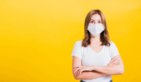 Portrait Asian beautiful young woman stand crossed arm wearing face mask protection filter dust pm2.5 anti-pollution, anti-smog, air pollution and COVID virus on a yellow background, with copy space