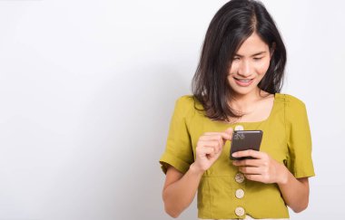 Asyalı güzel mutlu bir kadının portresi. Elinde cep telefonu, akıllı telefon kullanarak gülümseyen beyaz arka planda bir stüdyoda fotoğraf çeken bir kadın.