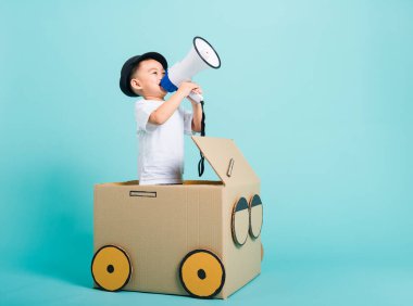 Mutlu Asyalı çocuk araba sürerken gülümse karton kutu hayal gücünün yanında megafonla, yaz tatili seyahat konseptiyle, stüdyoda çekilen metin için mavi arka planda
