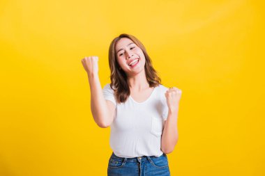 Asya Tayland mutlu portresi ayakta duran güzel hoş genç kadın tişört giyiyor. Kazanan yumruklarını kaldırıyor. Başarısını kutluyor.