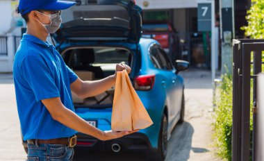 Asyalı genç teslimatçı kurye yemek siparişi için paket kağıdı konteynırlarıyla çevrimiçi, koruyucu yüz maskesi, sokağa çıkma yasağı altındaki ön evde servis müşterisi karantina altındaki Coronavirus COVID-19