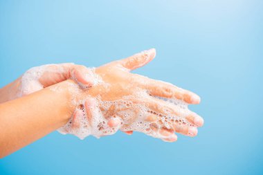 Kapalı vücut bakımı Asyalı genç kadın ellerini sabunla yıkıyor köpük, hijyen önleme COVID-19 veya koronavirüs koruma konsepti var, mavi arka planda izole edilmiş.