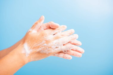 Kapalı vücut bakımı Asyalı genç kadın ellerini sabunla yıkıyor köpük, hijyen önleme COVID-19 veya koronavirüs koruma konsepti var, mavi arka planda izole edilmiş.