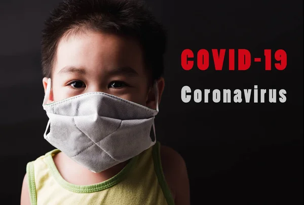 Closeup Asian little child wearing protective face mask with fear in the eye, prevent germs or disease hygiene prevention COVID-19 virus or coronavirus protection concept, dark on black background