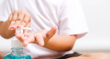 Kapalı kapılar ardında oturan küçük Asyalı çocuk şişe pompası dezenfekte edici jel temizleme, el yıkama, COVID-19 veya koronavirüs koruma konsepti, beyaz arka planda izole edilmiş fotokopi alanı