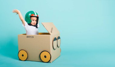 Miğferli mutlu Asyalı çocuk araba sürerken gülümsüyor. Karton kutu hayal gücü, yaz tatili seyahat konsepti, mavi arka planda çekimler, metin için metin alanı.