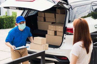 Asyalı genç teslimatçı kurye internetten alışveriş yapıyor koruyucu yüz maskesi ve servis görevlisi kadın müşteri sokağa çıkma yasağı altındaki evlerinin kapısında kutulanıyor, Coronavirus COVID-19