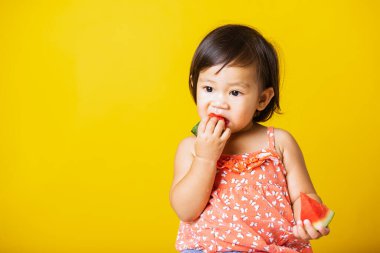 Mutlu portre Asyalı bebek ya da çocuk sevimli küçük kız gülüşü tişört giyen, yemek için kesilmiş karpuz tutan, sarı arka planda izole edilmiş stüdyo çekimi, sağlıklı yemek ve yaz konsepti