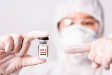 PPE üniformalı Asyalı kadın doktor veya hemşire ve yüz maskesi takan eldivenler laboratuvar ilaç şişesi Coronavirus aşı şişesinde ve şişesinde 